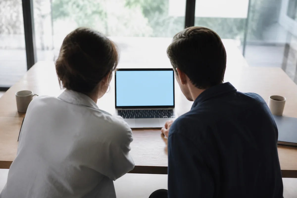 Deux personnes de dos face à un écran de portable affichant un formulaire vierge, bureau lumineux
